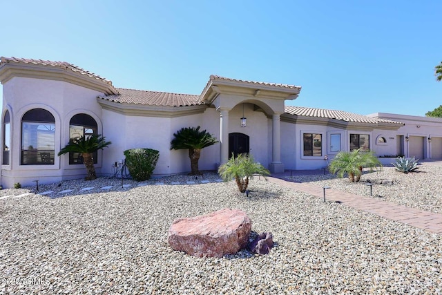 mediterranean / spanish-style home featuring stucco siding, a tile roof, and a garage