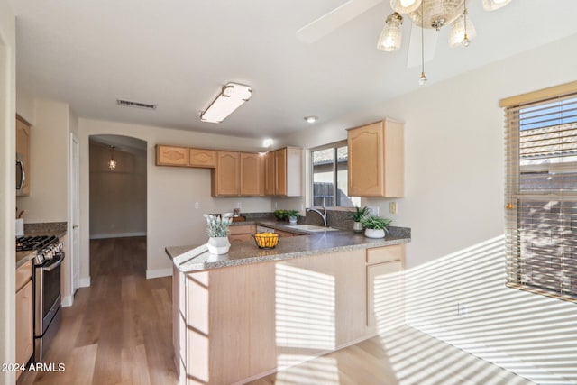 kitchen with sink, stainless steel gas range, kitchen peninsula, light brown cabinetry, and light wood-type flooring