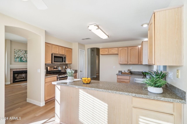 kitchen featuring light brown cabinets, sink, light hardwood / wood-style flooring, a fireplace, and appliances with stainless steel finishes