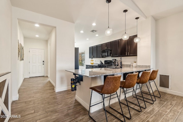 kitchen with pendant lighting, a kitchen breakfast bar, light stone counters, light hardwood / wood-style floors, and black appliances