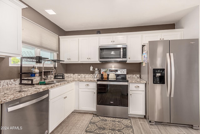 kitchen with white cabinets, light stone countertops, sink, light hardwood / wood-style floors, and stainless steel appliances