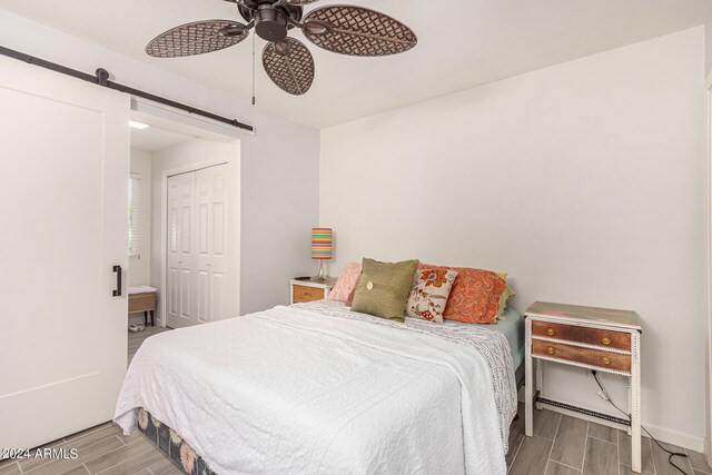 bedroom with hardwood / wood-style floors, a barn door, a closet, and ceiling fan