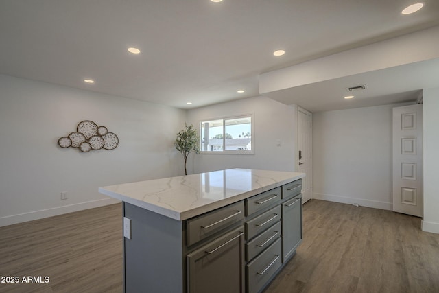 kitchen featuring hardwood / wood-style flooring, a center island, light stone counters, and gray cabinetry