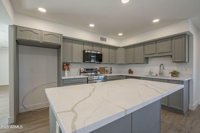 kitchen featuring sink, a center island, appliances with stainless steel finishes, dark hardwood / wood-style floors, and light stone countertops