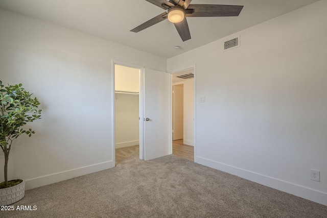 unfurnished bedroom featuring a spacious closet, light carpet, ceiling fan, and a closet