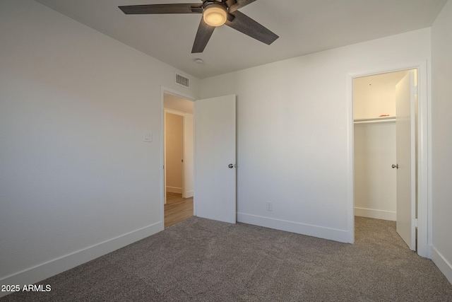 unfurnished bedroom featuring a walk in closet, light colored carpet, a closet, and ceiling fan