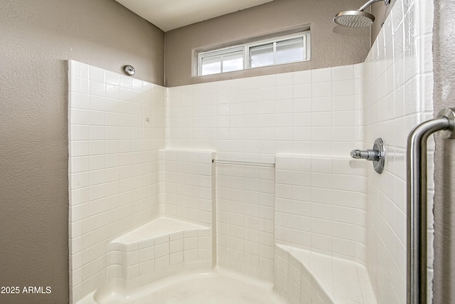 bathroom with a textured wall and tiled shower