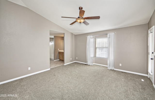 unfurnished bedroom with visible vents, light carpet, connected bathroom, baseboards, and vaulted ceiling