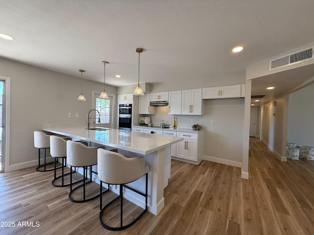 2337 E Manhatton Dr, Tempe, AZ 85282 - kitchen with a sink, a breakfast bar, white cabinets, under cabinet range hood, and baseboards