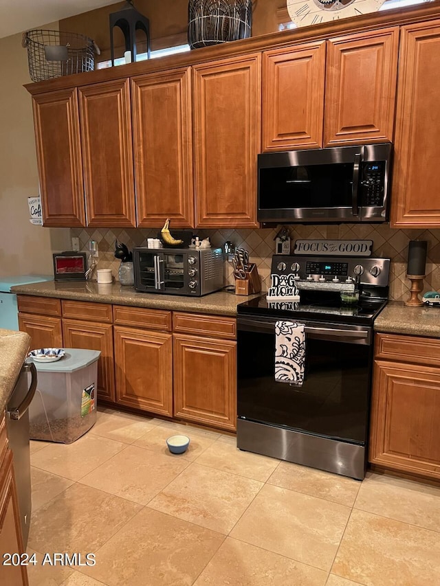 kitchen with stainless steel microwave, backsplash, brown cabinets, and black / electric stove