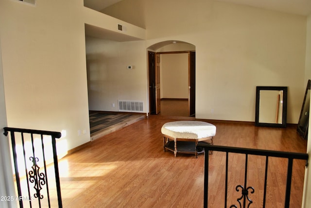 interior space featuring arched walkways, lofted ceiling, visible vents, baseboards, and light wood finished floors