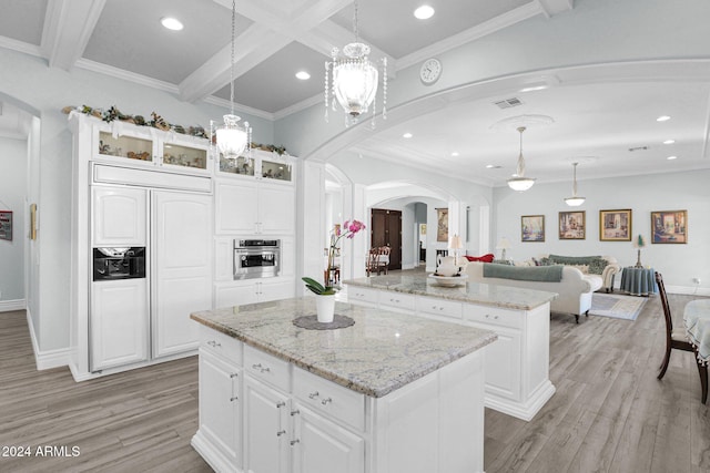 kitchen with decorative light fixtures, beamed ceiling, white cabinets, a center island, and oven