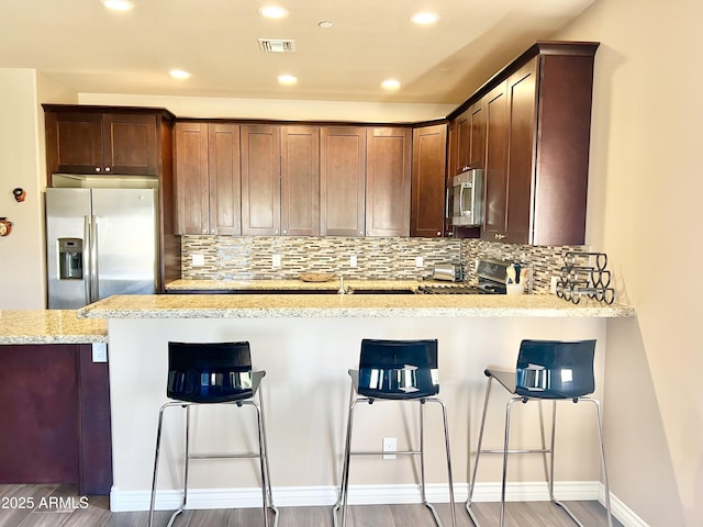 6145 E Cave Creek Rd Unit 203, Cave Creek, AZ 85331 - kitchen featuring stainless steel appliances, light wood-style flooring, a peninsula, tasteful backsplash, and a breakfast bar area