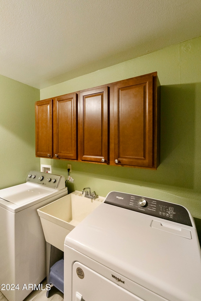 laundry area featuring a textured ceiling, washer and dryer, and cabinets