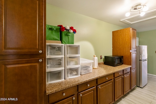 kitchen with light stone counters, stainless steel refrigerator, and light hardwood / wood-style flooring