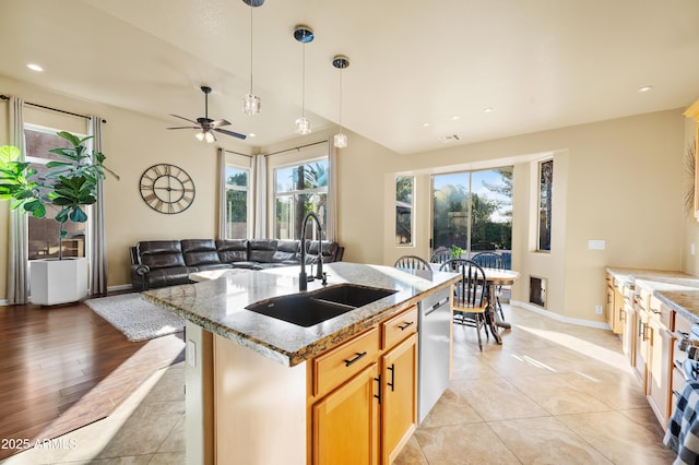 kitchen with pendant lighting, sink, stainless steel dishwasher, light stone countertops, and a center island with sink