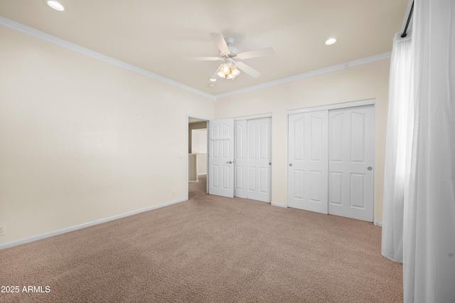 unfurnished bedroom featuring crown molding, light colored carpet, multiple closets, and ceiling fan