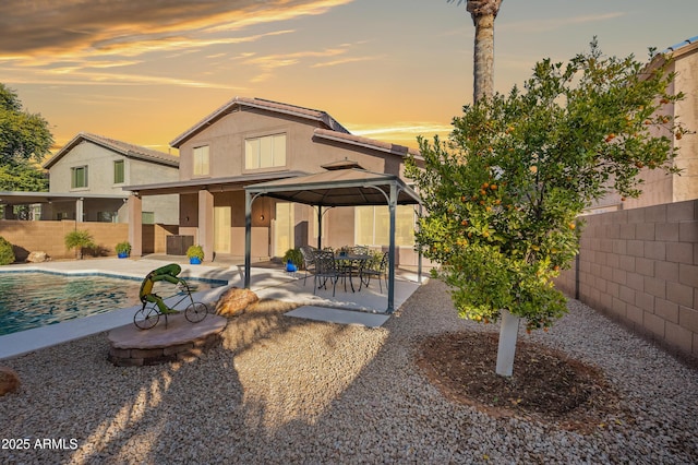 back house at dusk with a gazebo, a fenced in pool, and a patio