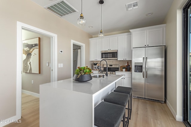 kitchen featuring white cabinets, appliances with stainless steel finishes, hanging light fixtures, and an island with sink