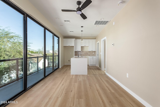 kitchen with light hardwood / wood-style floors, an island with sink, white cabinets, pendant lighting, and decorative backsplash