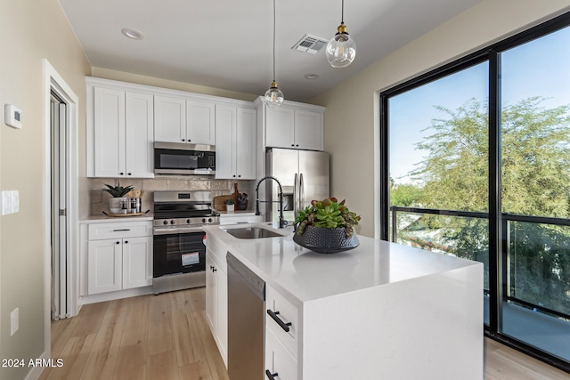 kitchen with stainless steel appliances, a center island with sink, sink, white cabinetry, and decorative light fixtures