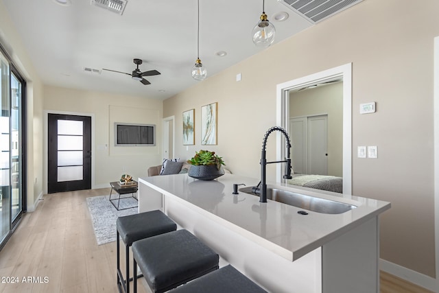 kitchen with sink, a kitchen island with sink, ceiling fan, light wood-type flooring, and decorative light fixtures