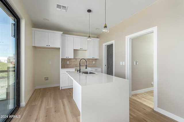 kitchen with white cabinetry, sink, decorative light fixtures, an island with sink, and light wood-type flooring