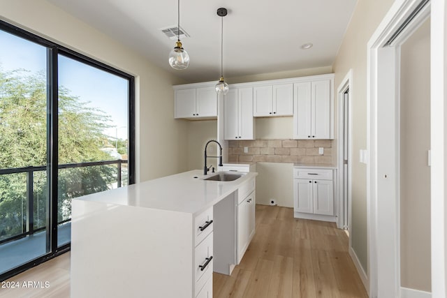 kitchen with white cabinetry, light wood-type flooring, decorative backsplash, sink, and an island with sink