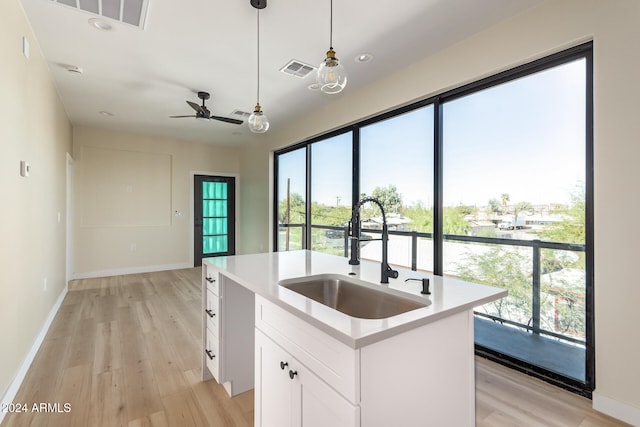 kitchen with a center island with sink, white cabinets, sink, pendant lighting, and light wood-type flooring