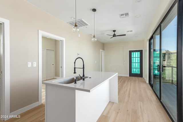 kitchen with decorative light fixtures, sink, an island with sink, ceiling fan, and light hardwood / wood-style flooring