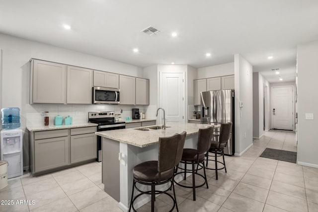 kitchen featuring a sink, appliances with stainless steel finishes, gray cabinetry, light stone counters, and tasteful backsplash