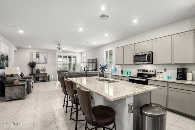 kitchen featuring stainless steel appliances, a sink, gray cabinetry, open floor plan, and light tile patterned floors
