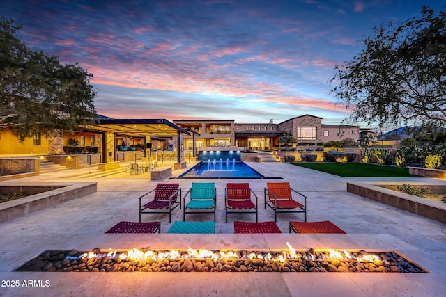 pool at dusk with pool water feature, a patio area, and an outdoor fire pit