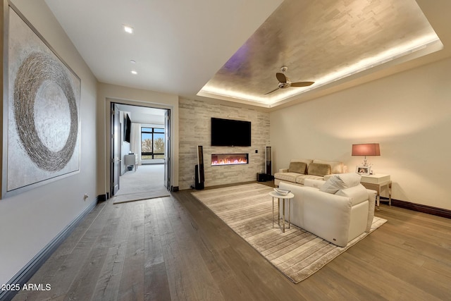 living room with ceiling fan, a large fireplace, light hardwood / wood-style flooring, and a tray ceiling