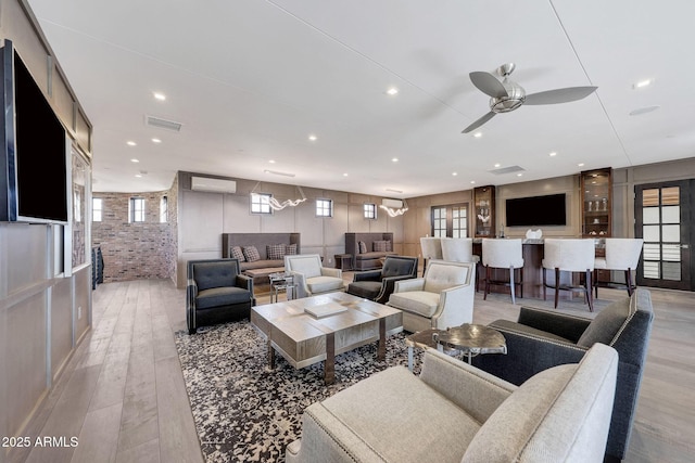 living room featuring ceiling fan with notable chandelier, an AC wall unit, and light hardwood / wood-style flooring