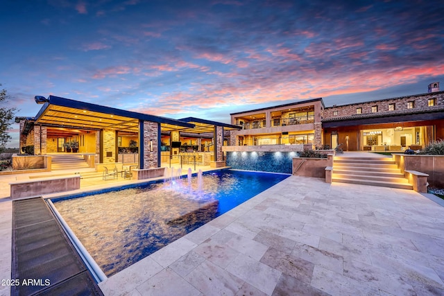 pool at dusk with pool water feature, a patio area, and a bar