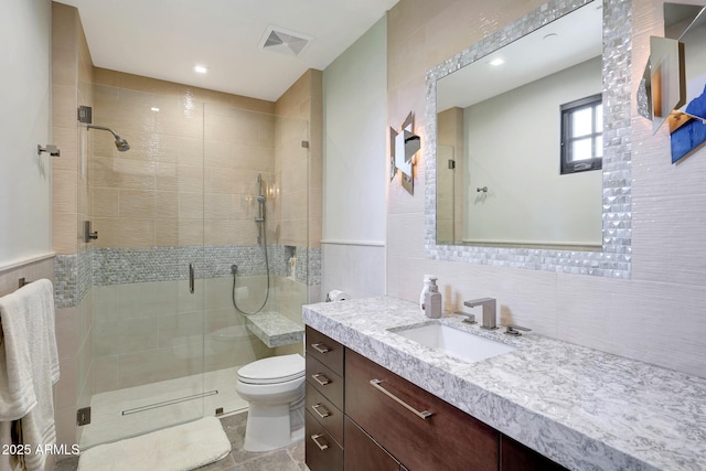 bathroom with vanity, toilet, a shower with door, and tile walls