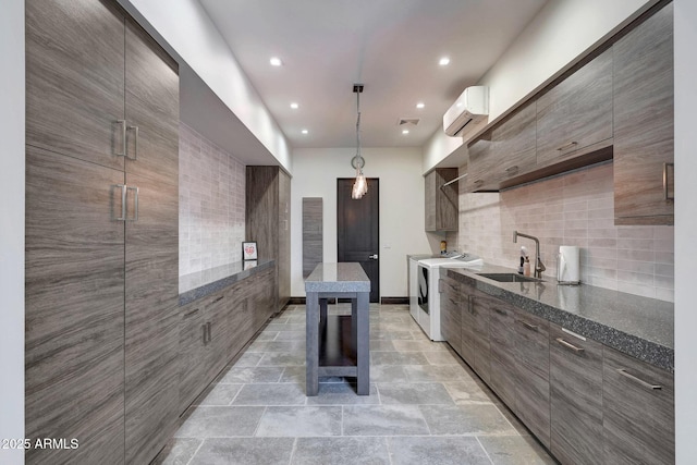 kitchen with pendant lighting, washer and clothes dryer, an AC wall unit, sink, and decorative backsplash