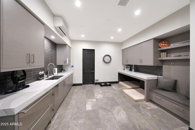 kitchen featuring sink, light stone counters, backsplash, a wall mounted AC, and gray cabinets