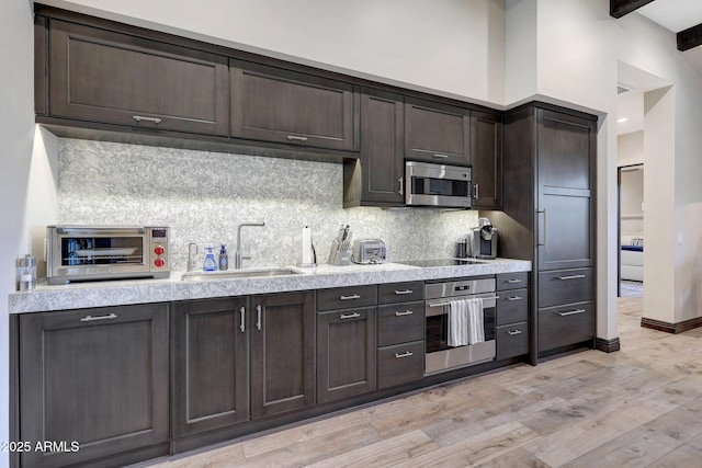 kitchen featuring dark brown cabinetry, sink, stainless steel appliances, light hardwood / wood-style flooring, and beamed ceiling