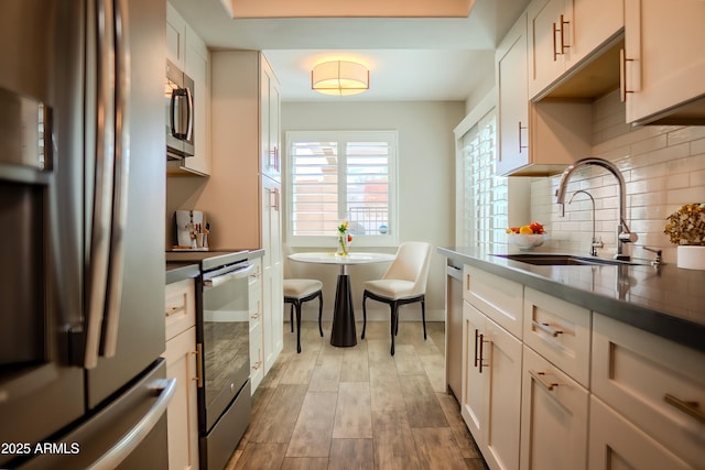 kitchen with sink, white cabinetry, appliances with stainless steel finishes, light hardwood / wood-style floors, and decorative backsplash