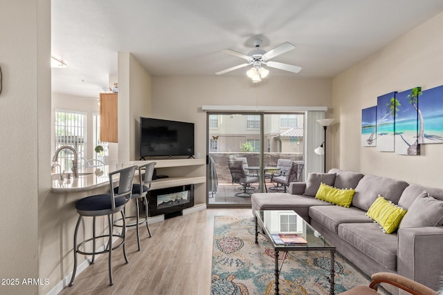 living room with light wood-style floors, baseboards, and a ceiling fan