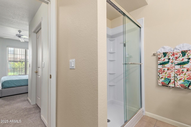 full bath featuring connected bathroom, a textured wall, ceiling fan, baseboards, and a shower stall
