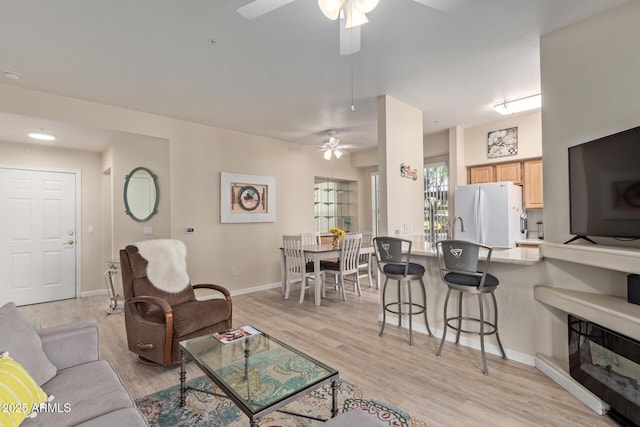 living area featuring baseboards, a ceiling fan, and light wood-style flooring