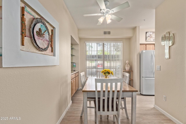 dining room with a textured wall, built in features, a ceiling fan, baseboards, and light wood-type flooring