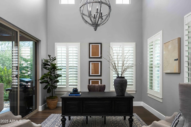 office featuring dark wood-type flooring, a towering ceiling, and a notable chandelier