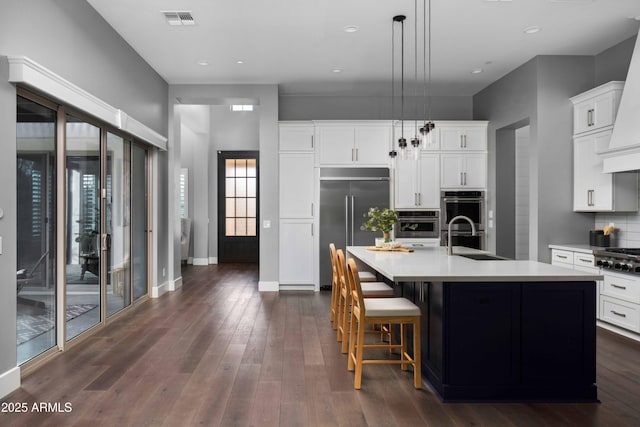 kitchen featuring an island with sink, appliances with stainless steel finishes, tasteful backsplash, hanging light fixtures, and sink