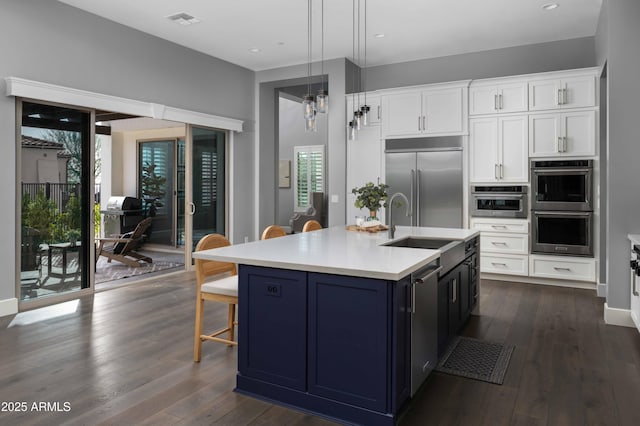 kitchen featuring stainless steel appliances, white cabinets, a center island with sink, and decorative light fixtures