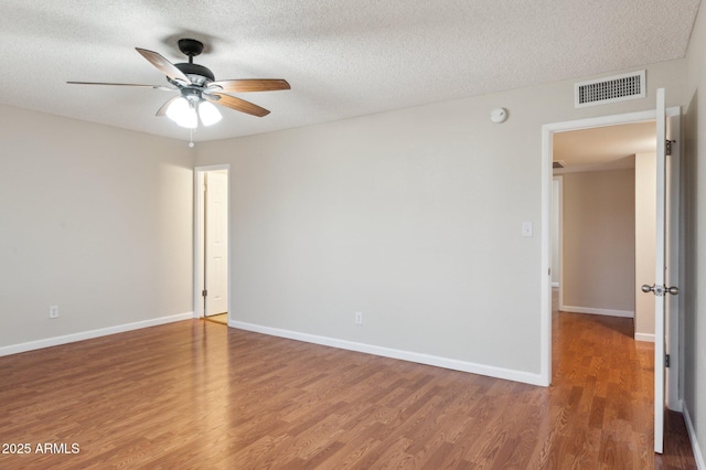 unfurnished room with a textured ceiling, wood finished floors, a ceiling fan, visible vents, and baseboards