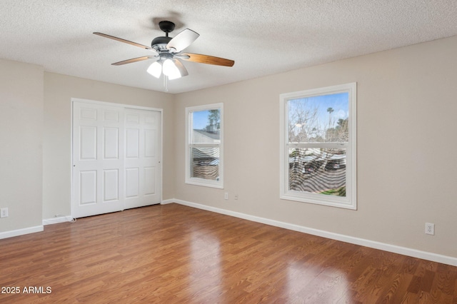 unfurnished bedroom featuring a textured ceiling, baseboards, and wood finished floors